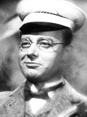Heinz Rühmann als Schüler Pfeiffer in „Die Feuerzangenbowle“, schwarzweiß, mit Schülermütze, runder Brille und Fliege